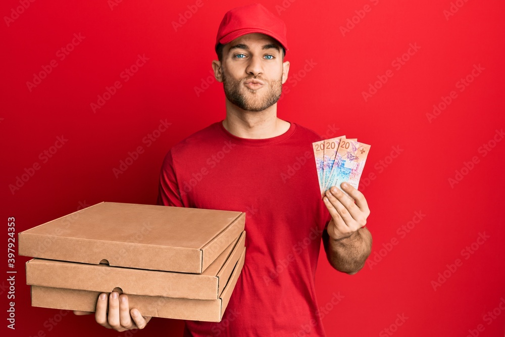 Young caucasian man holding delivery box and swiss franc banknotes looking at the camera blowing a kiss being lovely and sexy. love expression. Young caucasian man holding delivery box and swiss franc banknotes looking at the camera blowing a kiss being lovely and sexy. love expression.