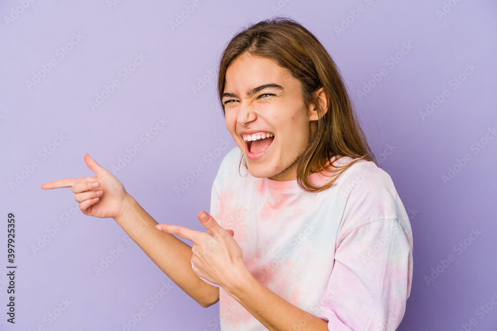 Young skinny caucasian girl teenager on purple background pointing with forefingers to a copy space, expressing excitement and desire. Young skinny caucasian girl teenager on purple background pointing with forefingers to a copy space, expressing excitement and desire.