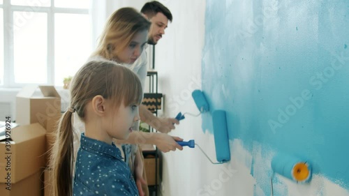 Young couple with child remodelling house painting wall and dancing enjoying music and repairs activity together. Youth and lifestyle concept.