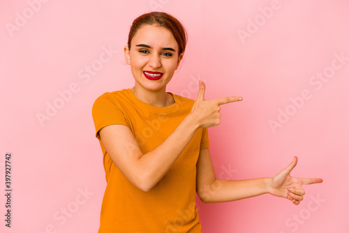 Young arab mixed race woman pointing with forefingers to a copy space  expressing excitement and desire.
