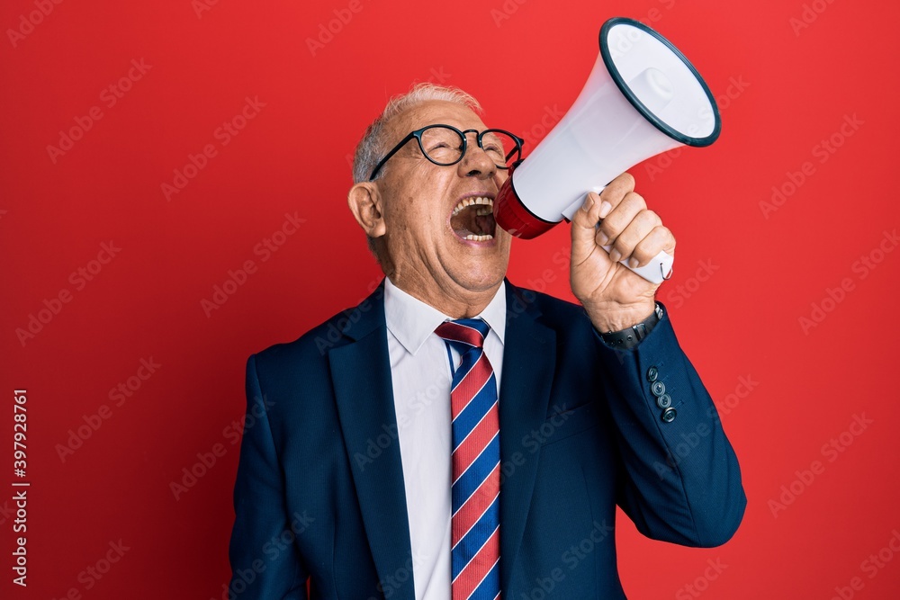 Senior grey-haired businessman screaming using megaphone over isolated red background. Senior grey-haired businessman screaming using megaphone over isolated red background.
