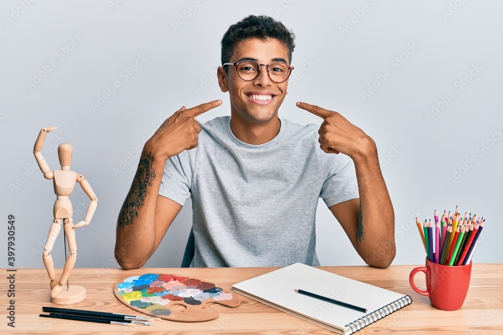 Young handsome african american man painter sitting palette and art manikin smiling cheerful showing and pointing with fingers teeth and mouth. dental health concept. Young handsome african american man painter sitting palette and art manikin smiling cheerful showing and pointing with fingers teeth and mouth. dental health concept.