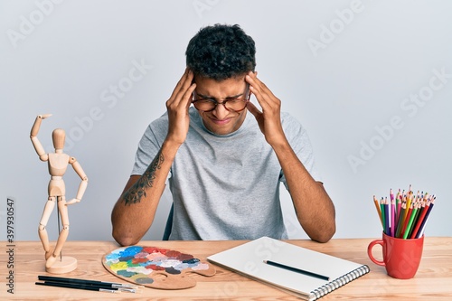 Young handsome african american man painter sitting palette and art manikin suffering from headache desperate and stressed because pain and migraine. hands on head.