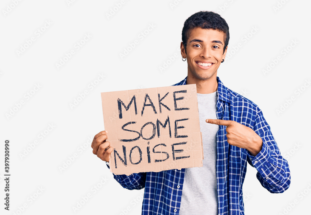 Young african amercian man holding make some noise banner smiling happy pointing with hand and finger Young african amercian man holding make some noise banner smiling happy pointing with hand and finger