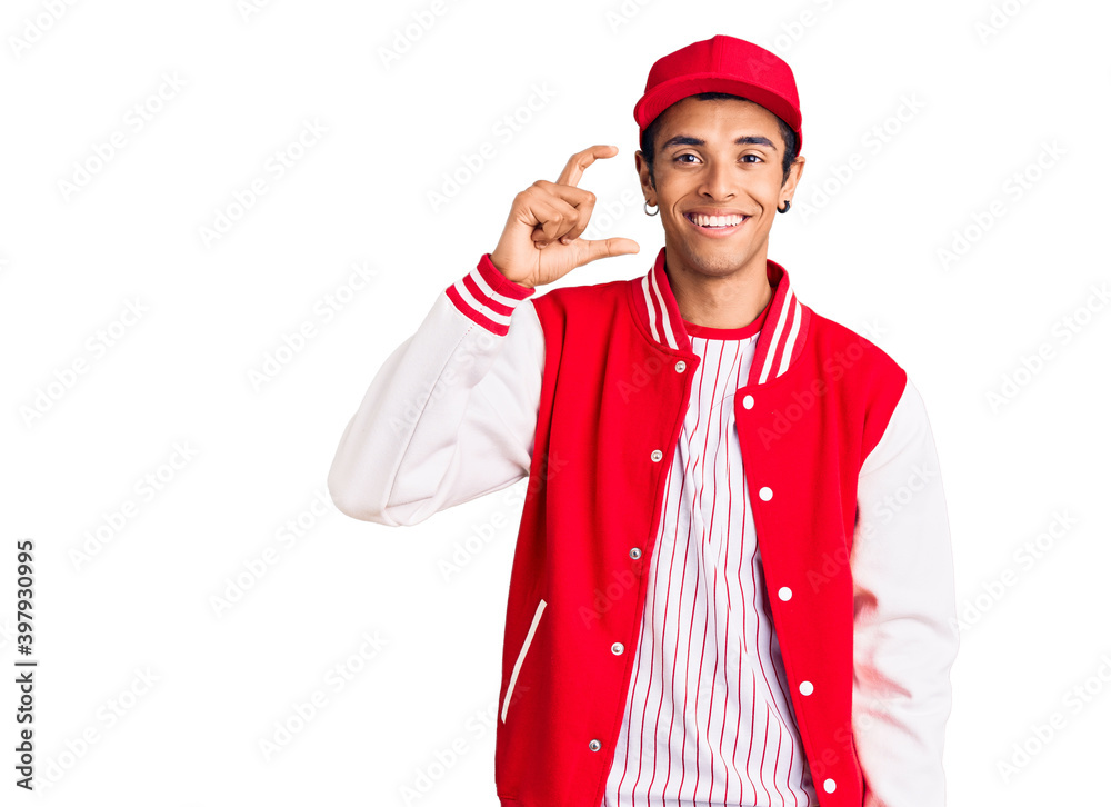 Young african amercian man wearing baseball uniform smiling and confident gesturing with hand doing small size sign with fingers looking and the camera. measure concept. Young african amercian man wearing baseball uniform smiling and confident gesturing with hand doing small size sign with fingers looking and the camera. measure concept.