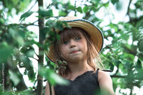 Little girl in a straw hat in the green park among the leaves.
