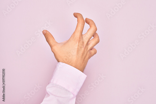 Hand of caucasian young man showing fingers over isolated pink background grasping aggressive and scary with fingers  violence and frustration