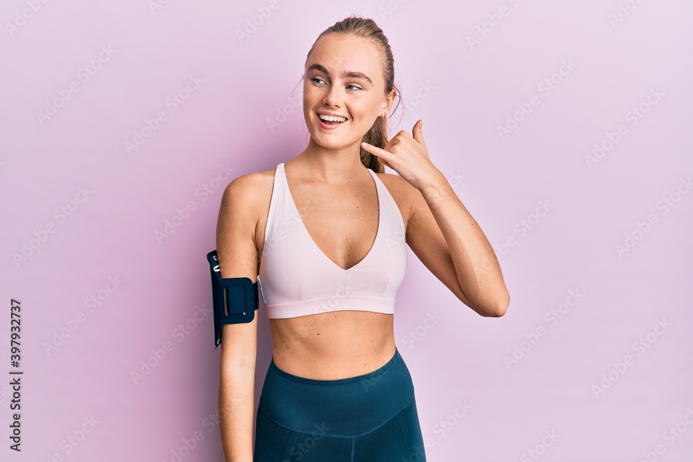 Beautiful blonde woman wearing sportswear and arm band smiling doing phone gesture with hand and fingers like talking on the telephone. communicating concepts.