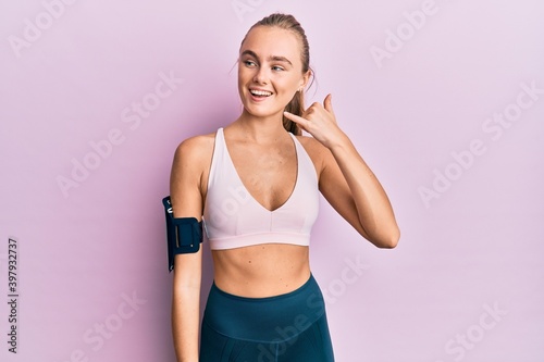 Beautiful blonde woman wearing sportswear and arm band smiling doing phone gesture with hand and fingers like talking on the telephone. communicating concepts. © Krakenimages.com