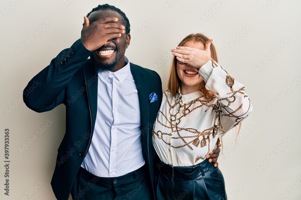 Young interracial couple wearing business and elegant clothes smiling and laughing with hand on face covering eyes for surprise. blind concept.
