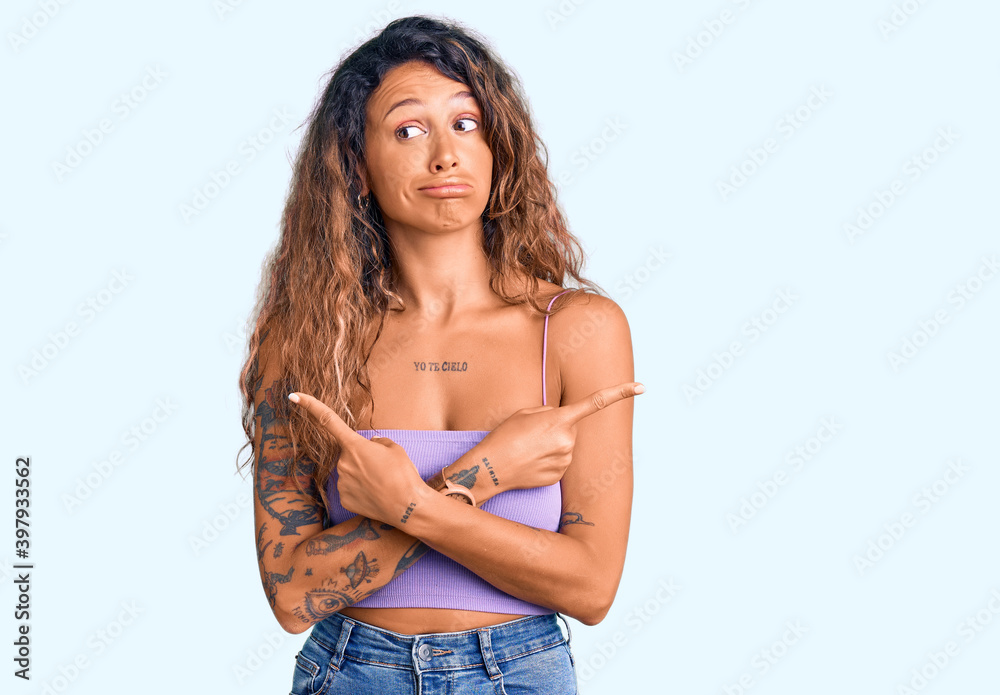 Young hispanic woman with tattoo wearing casual clothes pointing to both sides with fingers, different direction disagree Young hispanic woman with tattoo wearing casual clothes pointing to both sides with fingers, different direction disagree