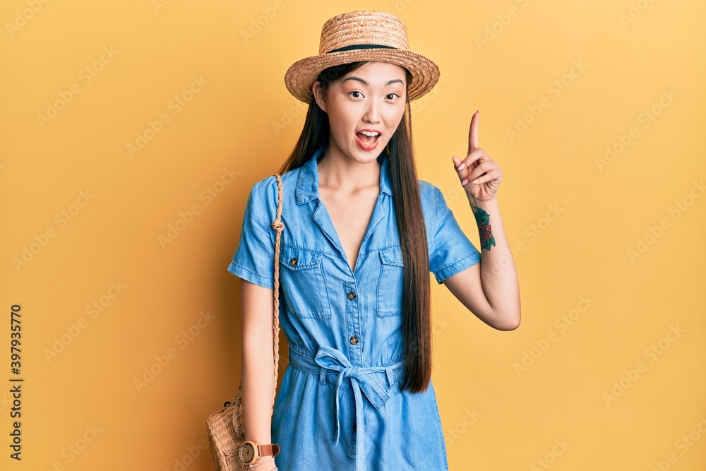 Young chinese woman wearing summer hat pointing finger up with successful idea. exited and happy. number one. Young chinese woman wearing summer hat pointing finger up with successful idea. exited and happy. number one.
