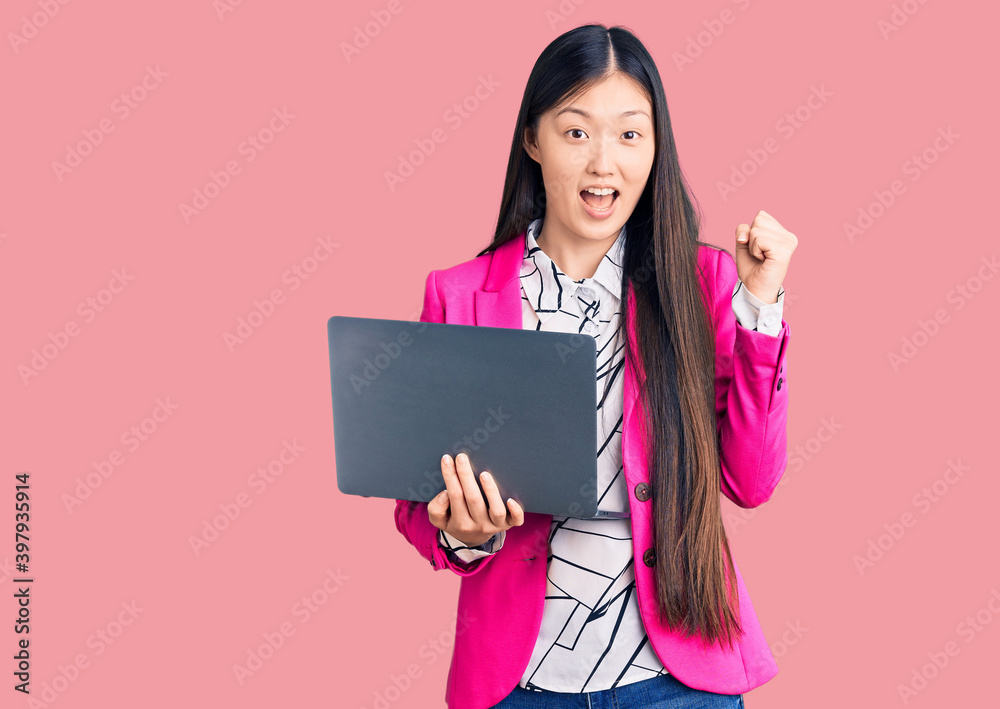 Young beautiful chinese woman using laptop screaming proud, celebrating victory and success very excited with raised arms Young beautiful chinese woman using laptop screaming proud, celebrating victory and success very excited with raised arms