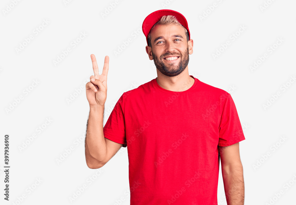 Naklejka premium Young handsome blond man wearing t-shirt and cap showing and pointing up with fingers number two while smiling confident and happy.