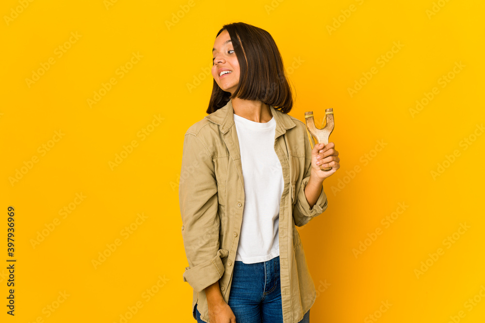 Young hispanic woman holding a slingshot looks aside smiling, cheerful and pleasant. Young hispanic woman holding a slingshot looks aside smiling, cheerful and pleasant.