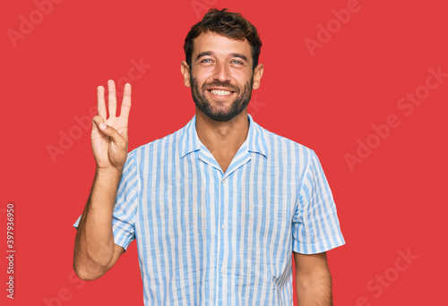 Handsome young man with beard wearing casual fresh shirt showing and pointing up with fingers number three while smiling confident and happy.