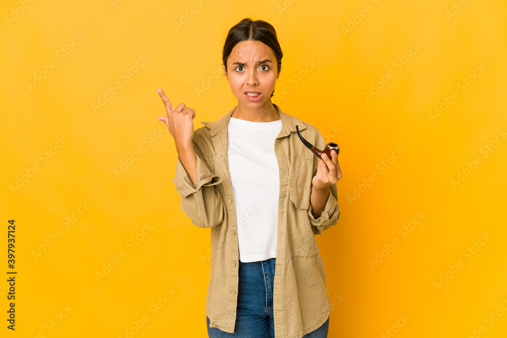 Young hispanic woman holding a smoking pipe showing a disappointment gesture with forefinger.