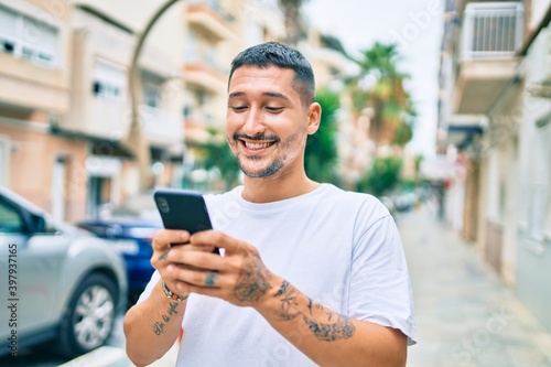 Young hispanic man smiling happy using smartphone at street of city.