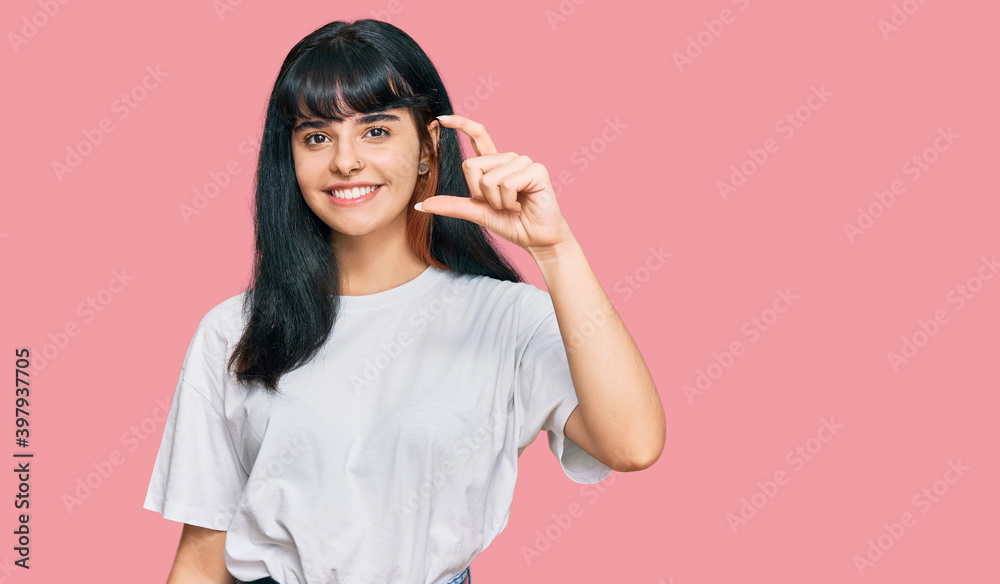 Young hispanic girl wearing casual clothes smiling and confident gesturing with hand doing small size sign with fingers looking and the camera. measure concept. Young hispanic girl wearing casual clothes smiling and confident gesturing with hand doing small size sign with fingers looking and the camera. measure concept.