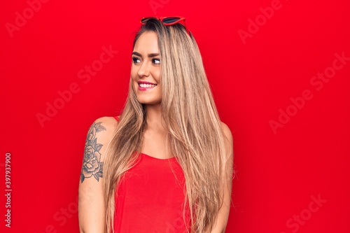 Young beautiful blonde woman wearing red t-shirt and sunglasses over isolated background looking to side, relax profile pose with natural face and confident smile.