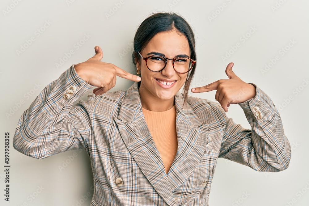 Young brunette woman wearing business jacket and glasses smiling cheerful showing and pointing with fingers teeth and mouth. dental health concept. Young brunette woman wearing business jacket and glasses smiling cheerful showing and pointing with fingers teeth and mouth. dental health concept.