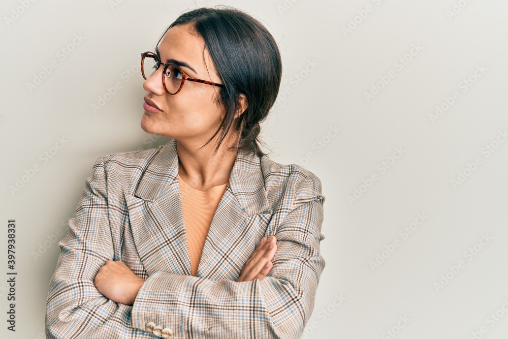 Young brunette woman wearing business jacket and glasses looking to the side with arms crossed convinced and confident Young brunette woman wearing business jacket and glasses looking to the side with arms crossed convinced and confident