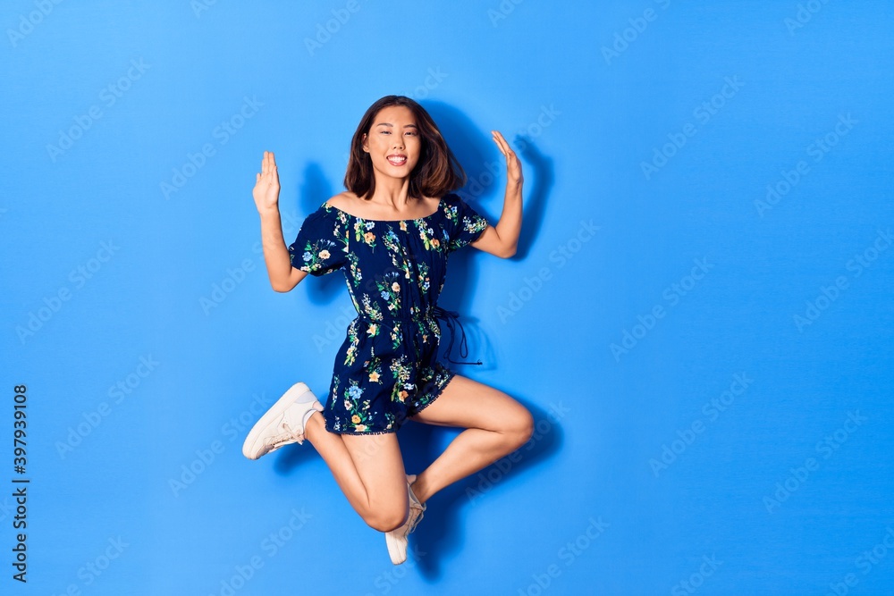 Young beautiful chinese woman wearing casual clothes smiling happy. Jumping with smile on face over isolated blue background Young beautiful chinese woman wearing casual clothes smiling happy. Jumping with smile on face over isolated blue background