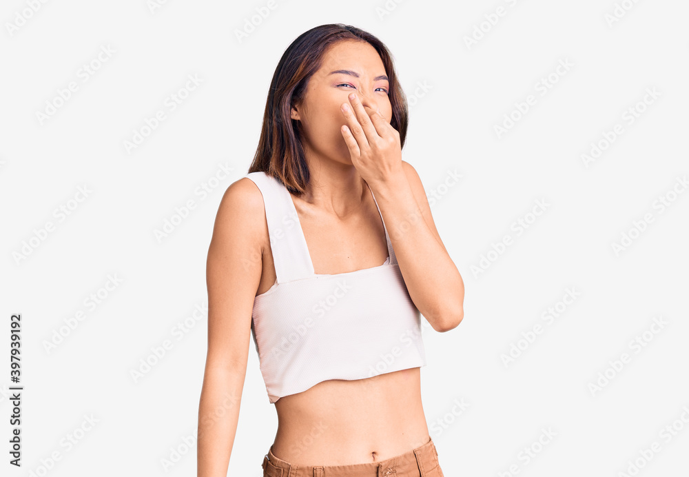 Young beautiful chinese girl wearing casual clothes smelling something stinky and disgusting, intolerable smell, holding breath with fingers on nose. bad smell Young beautiful chinese girl wearing casual clothes smelling something stinky and disgusting, intolerable smell, holding breath with fingers on nose. bad smell