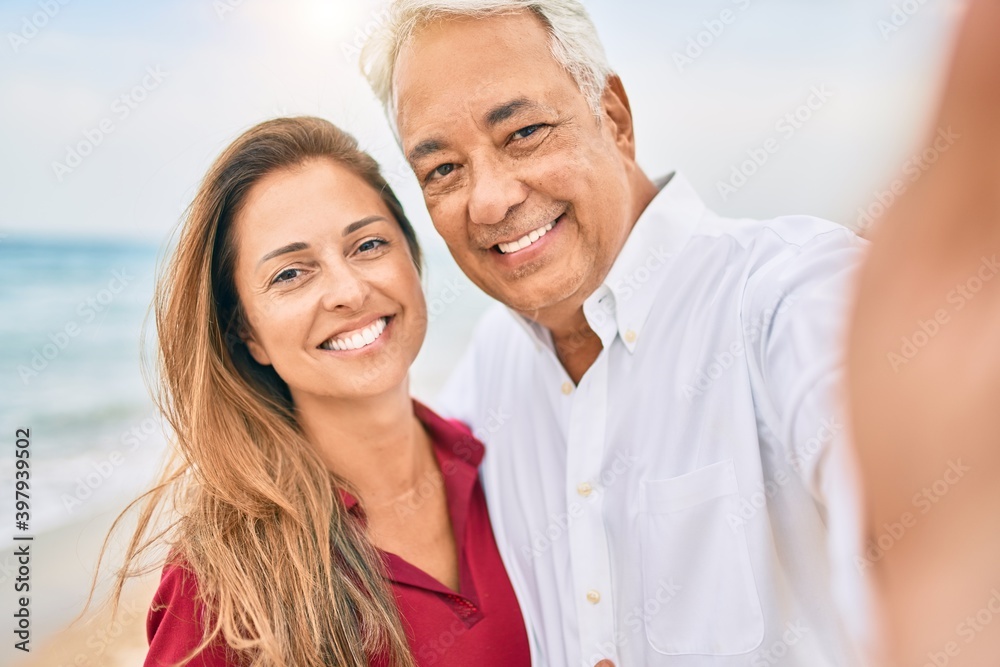 Middle age hispanic couple smiling happy making selfie by the camera at the beach. Middle age hispanic couple smiling happy making selfie by the camera at the beach.
