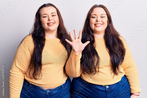 Young plus size twins wearing casual clothes showing and pointing up with fingers number five while smiling confident and happy.