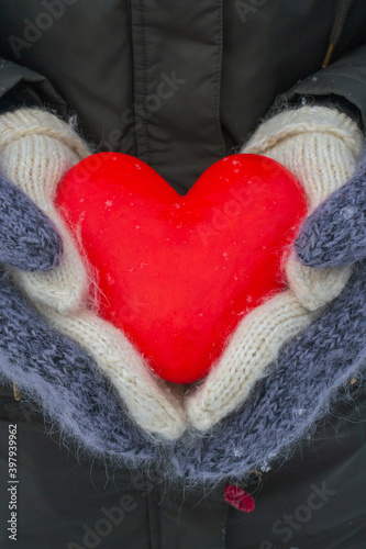 Festive postcard. Female and male hands in fluffy mittens hold a red heart. Valentine s day concept.