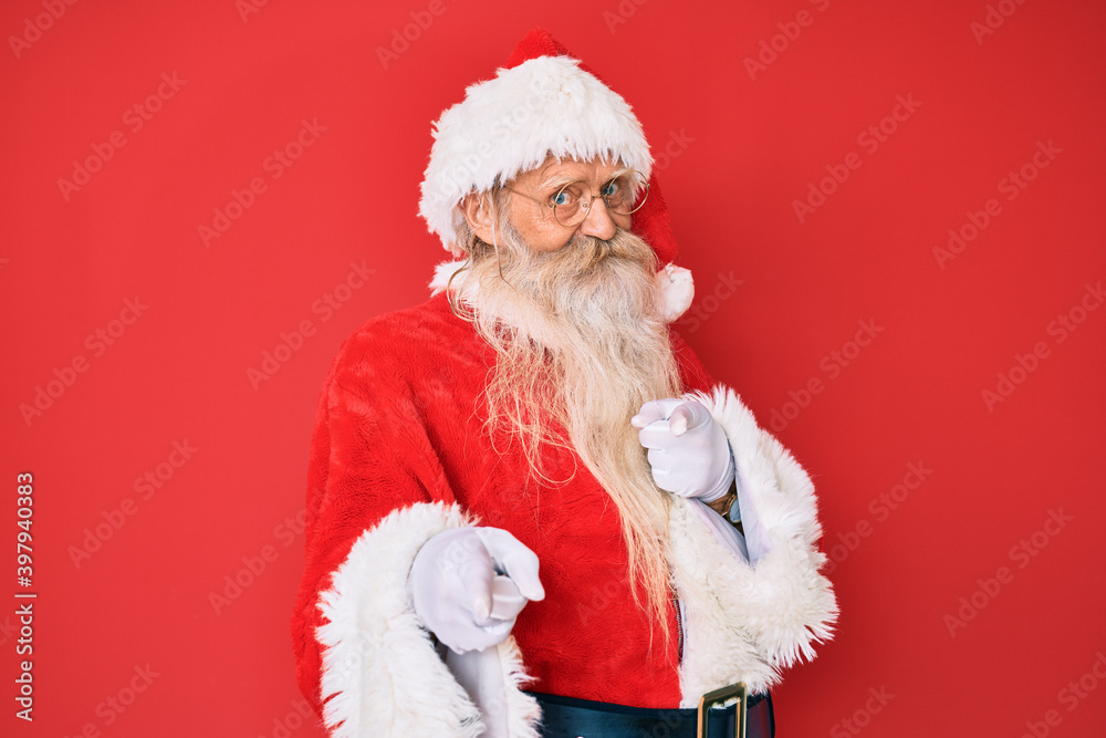 Old senior man with grey hair and long beard wearing traditional santa claus costume pointing fingers to camera with happy and funny face. good energy and vibes. Old senior man with grey hair and long beard wearing traditional santa claus costume pointing fingers to camera with happy and funny face. good energy and vibes.