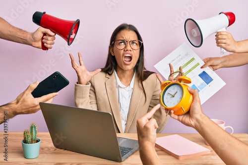 Beautiful hispanic woman working at the office under stress crazy and mad shouting and yelling with aggressive expression and arms raised. frustration concept.