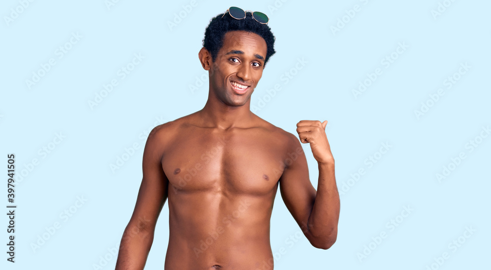 African handsome man wearing swimsuit and sunglasses smiling with happy face looking and pointing to the side with thumb up. African handsome man wearing swimsuit and sunglasses smiling with happy face looking and pointing to the side with thumb up.