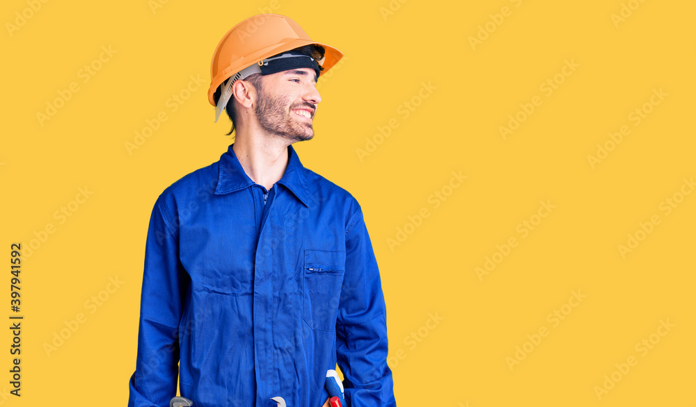 Young hispanic man wearing worker uniform looking away to side with smile on face, natural expression. laughing confident.