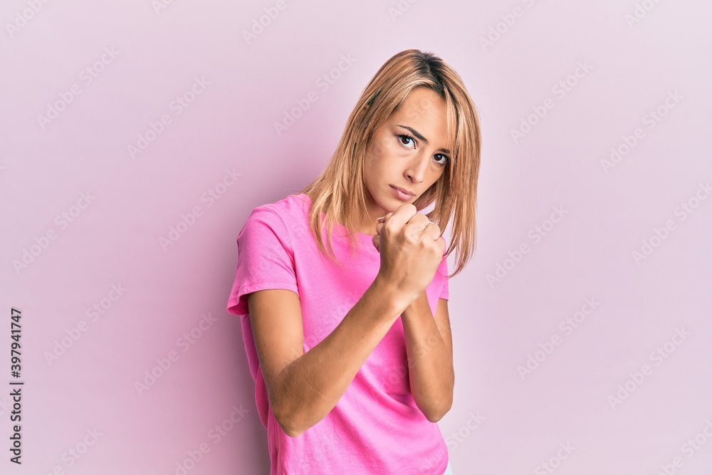 Beautiful blonde woman wearing casual pink tshirt ready to fight with fist defense gesture, angry and upset face, afraid of problem Beautiful blonde woman wearing casual pink tshirt ready to fight with fist defense gesture, angry and upset face, afraid of problem