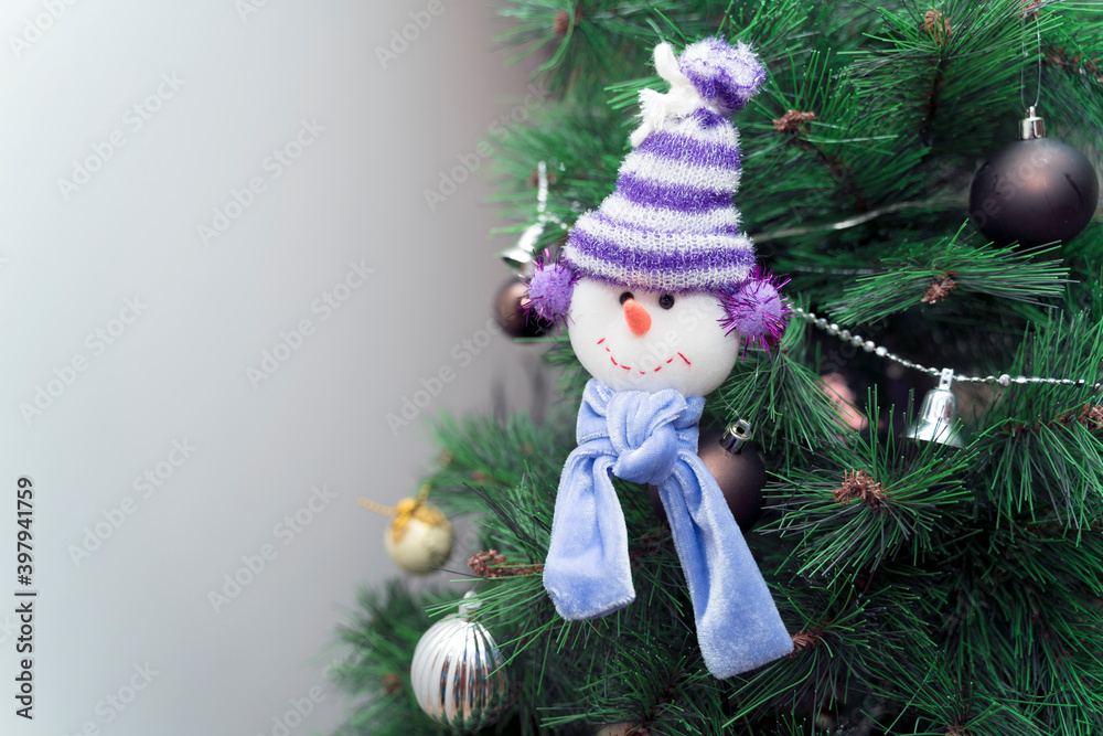 Fabric snowman decorating the Christmas tree with colored balls and merry Christmas 2021 ornaments. Space for text
