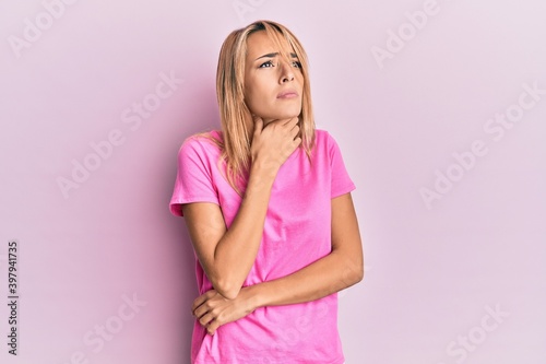 Beautiful blonde woman wearing casual pink tshirt touching painful neck  sore throat for flu  clod and infection