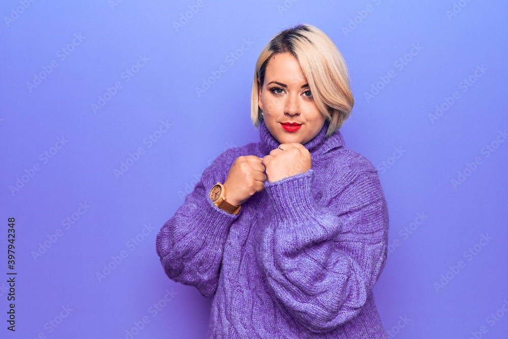 Beautiful blonde plus size woman wearing casual turtleneck sweater over purple background Ready to fight with fist defense gesture, angry and upset face, afraid of problem Beautiful blonde plus size woman wearing casual turtleneck sweater over purple background Ready to fight with fist defense gesture, angry and upset face, afraid of problem