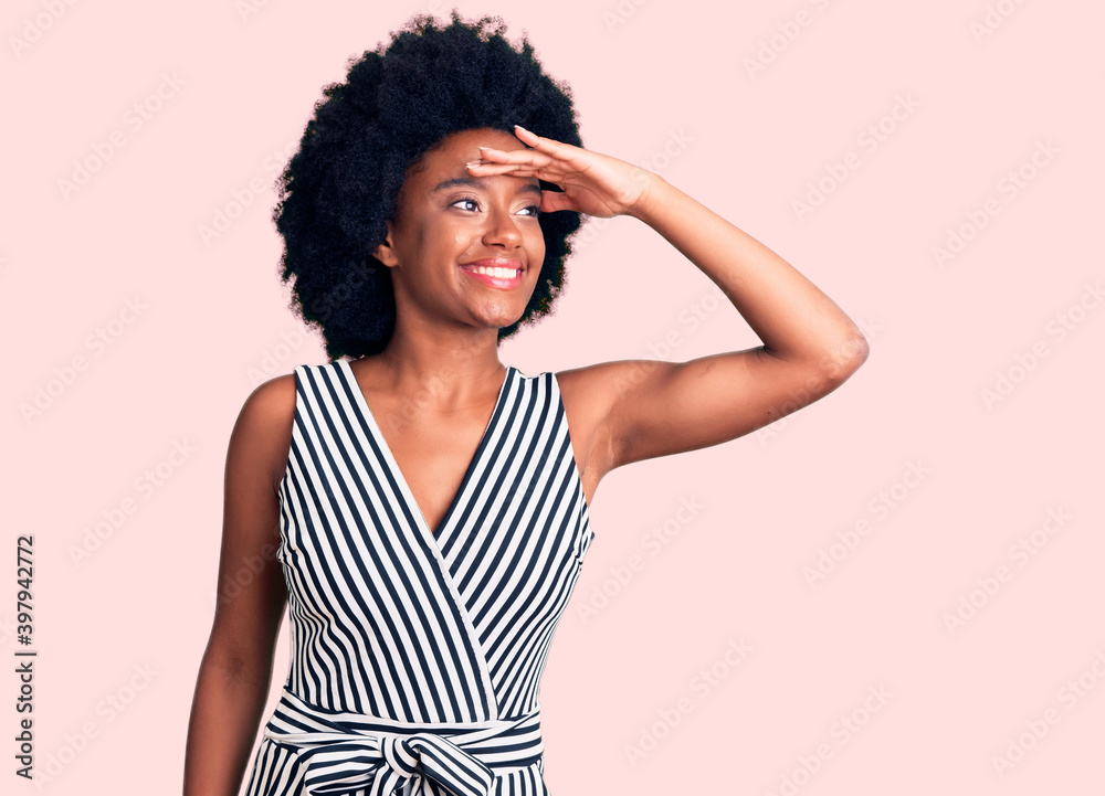Young african american woman wearing casual clothes very happy and smiling looking far away with hand over head. searching concept. Young african american woman wearing casual clothes very happy and smiling looking far away with hand over head. searching concept.