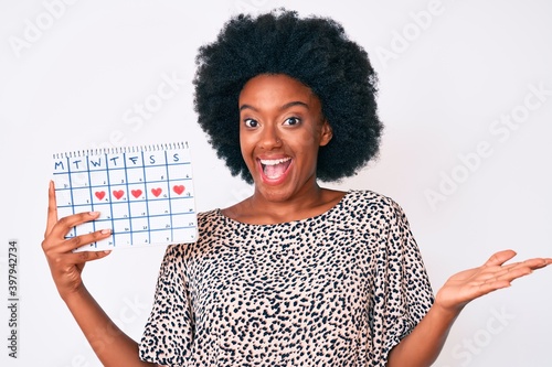 Young african american woman holding heart calendar celebrating achievement with happy smile and winner expression with raised hand photo