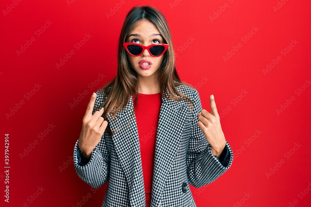 Young brunette woman wearing fashion and modern look amazed and surprised looking up and pointing with fingers and raised arms. Young brunette woman wearing fashion and modern look amazed and surprised looking up and pointing with fingers and raised arms.