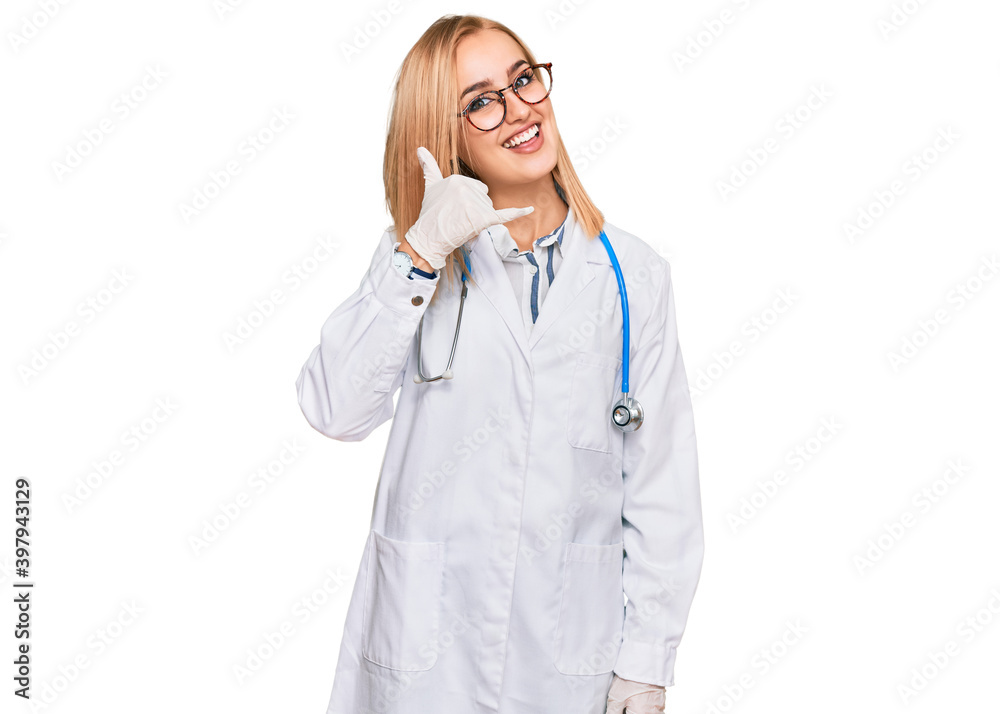 Beautiful caucasian woman wearing doctor uniform and stethoscope smiling doing phone gesture with hand and fingers like talking on the telephone. communicating concepts. Beautiful caucasian woman wearing doctor uniform and stethoscope smiling doing phone gesture with hand and fingers like talking on the telephone. communicating concepts.