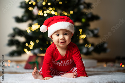 adorable little baby boy in a santa costume sitting on a soft fake fur in front of a christmas tree
