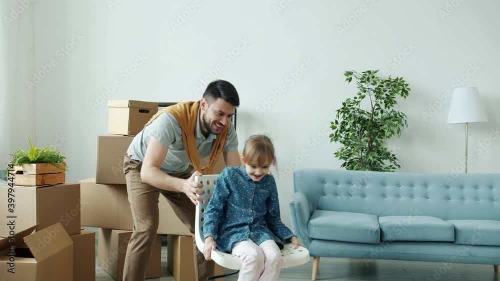 Caring dad is having fun with little daughter pushing chair with kid tickling laughing in new house. Happy childhood and family relocation concept. Caring dad is having fun with little daughter pushing chair with kid tickling laughing in new house. Happy childhood and family relocation concept.