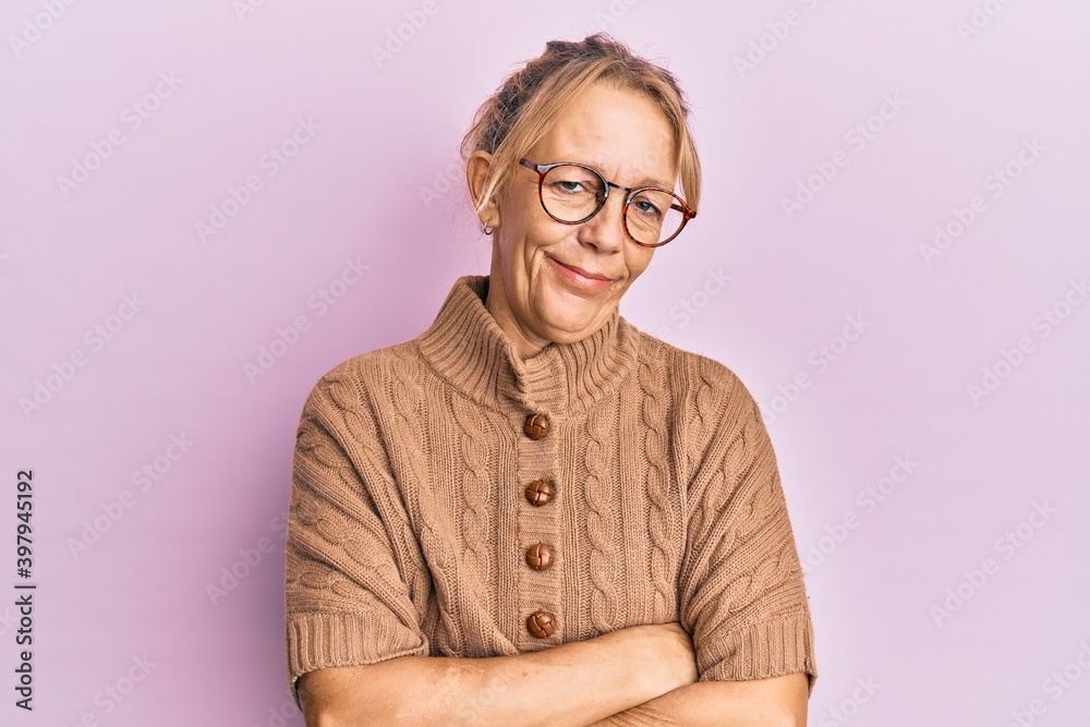 Middle age blonde woman wearing glasses over pink background happy face smiling with crossed arms looking at the camera. positive person.