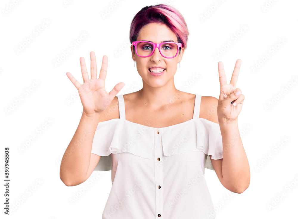 Young beautiful woman with pink hair wearing casual clothes and glasses showing and pointing up with fingers number seven while smiling confident and happy. Young beautiful woman with pink hair wearing casual clothes and glasses showing and pointing up with fingers number seven while smiling confident and happy.