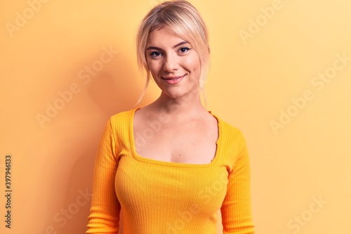 Young beautiful blonde woman wearing casual t-shirt standing over isolated yellow background with a happy and cool smile on face. Lucky person.
