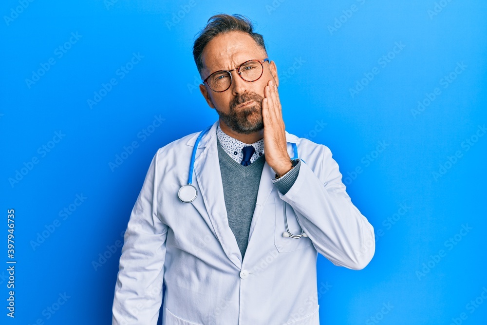 Handsome middle age man wearing doctor uniform and stethoscope touching mouth with hand with painful expression because of toothache or dental illness on teeth. dentist Handsome middle age man wearing doctor uniform and stethoscope touching mouth with hand with painful expression because of toothache or dental illness on teeth. dentist