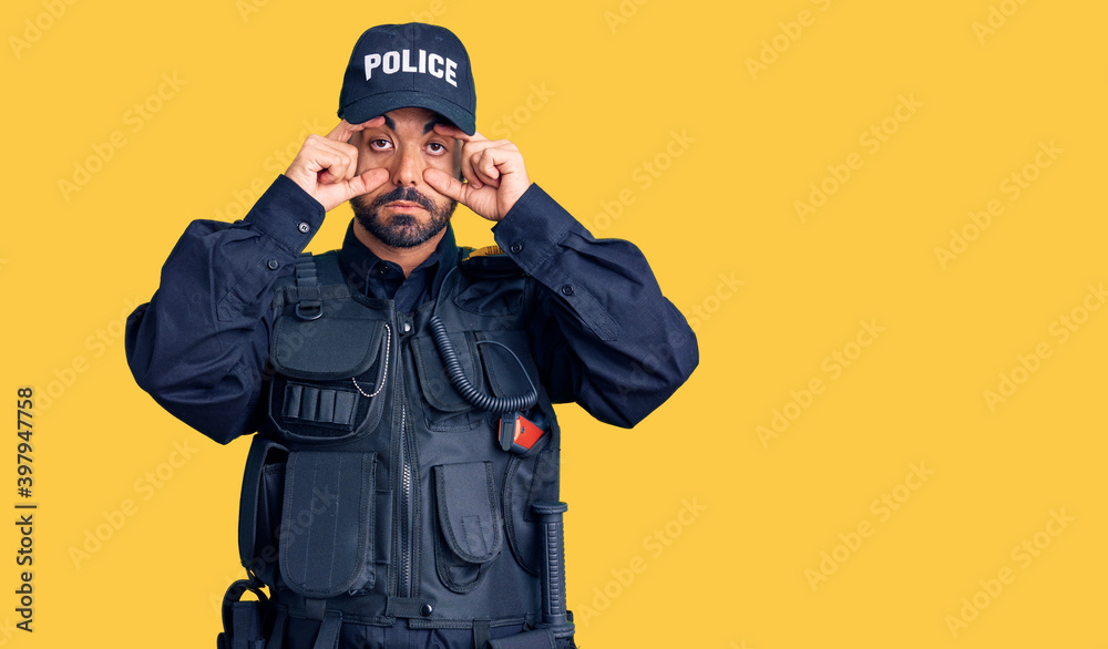 Young hispanic man wearing police uniform trying to open eyes with fingers, sleepy and tired for morning fatigue Young hispanic man wearing police uniform trying to open eyes with fingers, sleepy and tired for morning fatigue